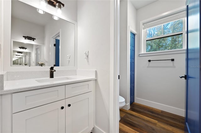 bathroom featuring toilet, baseboards, wood finished floors, and vanity