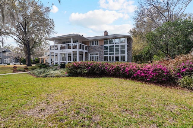 back of property with stone siding, a lawn, a chimney, and a balcony