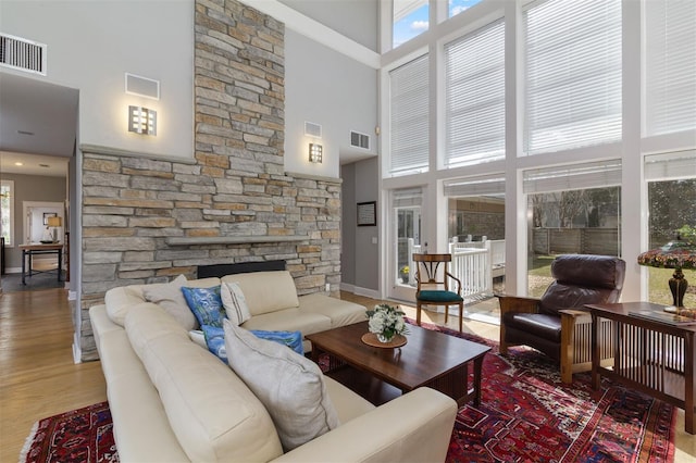 living area featuring a stone fireplace, a high ceiling, wood finished floors, and visible vents