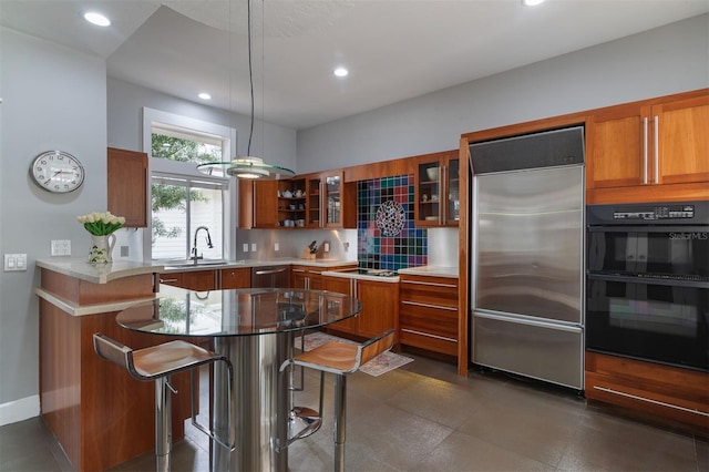 kitchen featuring a sink, a kitchen breakfast bar, appliances with stainless steel finishes, brown cabinetry, and glass insert cabinets