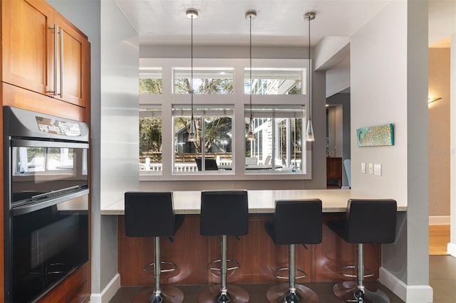 kitchen featuring a breakfast bar, multiple ovens, brown cabinets, and baseboards