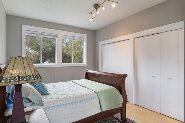 bedroom with light wood-style floors, track lighting, and two closets