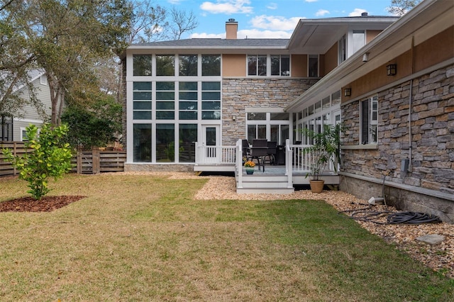 back of house featuring stone siding, a lawn, a wooden deck, and fence