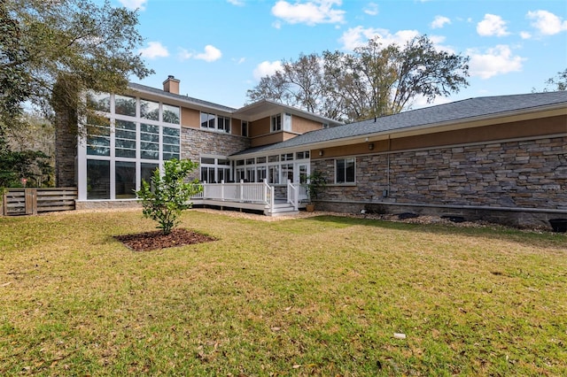 back of property with a deck, fence, a yard, stone siding, and a chimney