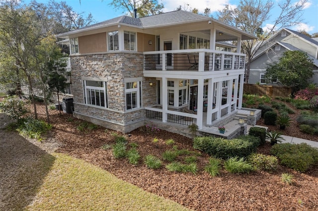 back of property with a balcony, stone siding, and stucco siding