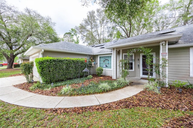 ranch-style house with a garage, roof with shingles, covered porch, and solar panels