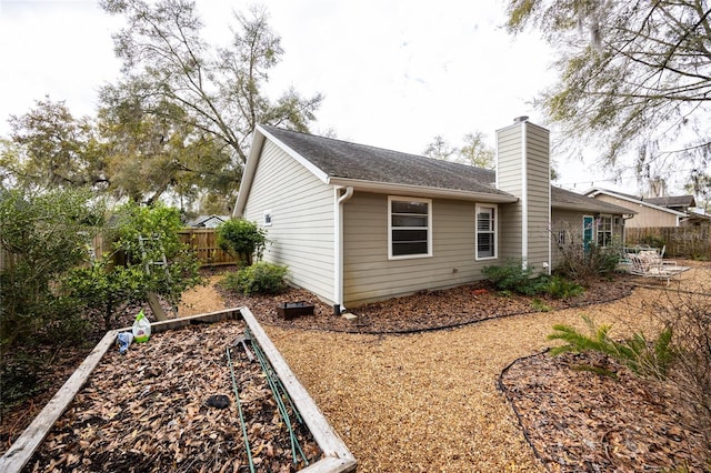 view of side of property featuring a vegetable garden, fence, and a chimney