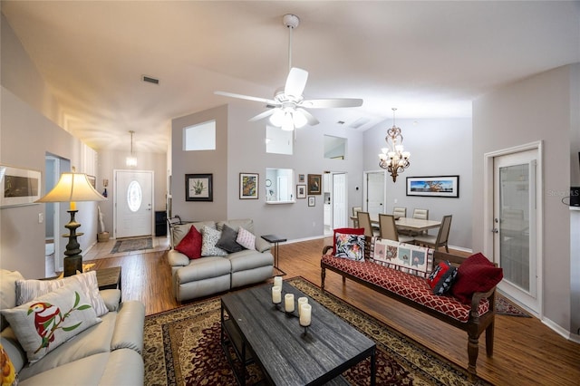 living room with visible vents, high vaulted ceiling, ceiling fan with notable chandelier, wood finished floors, and baseboards