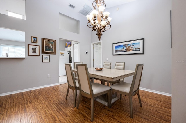 dining space featuring a notable chandelier, wood finished floors, baseboards, and a towering ceiling