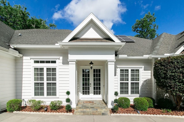 view of exterior entry featuring a shingled roof, roof mounted solar panels, and french doors