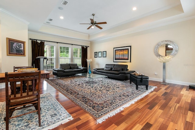 living room featuring baseboards, visible vents, a raised ceiling, ornamental molding, and wood finished floors