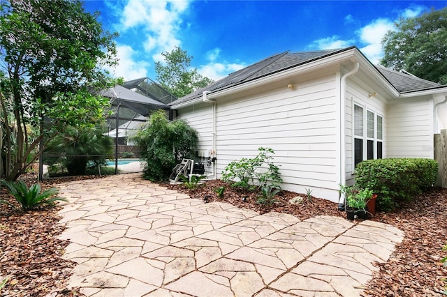 view of side of home featuring a shingled roof, a lanai, a patio, and an outdoor pool