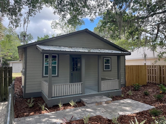 view of front facade featuring covered porch, fence, and metal roof