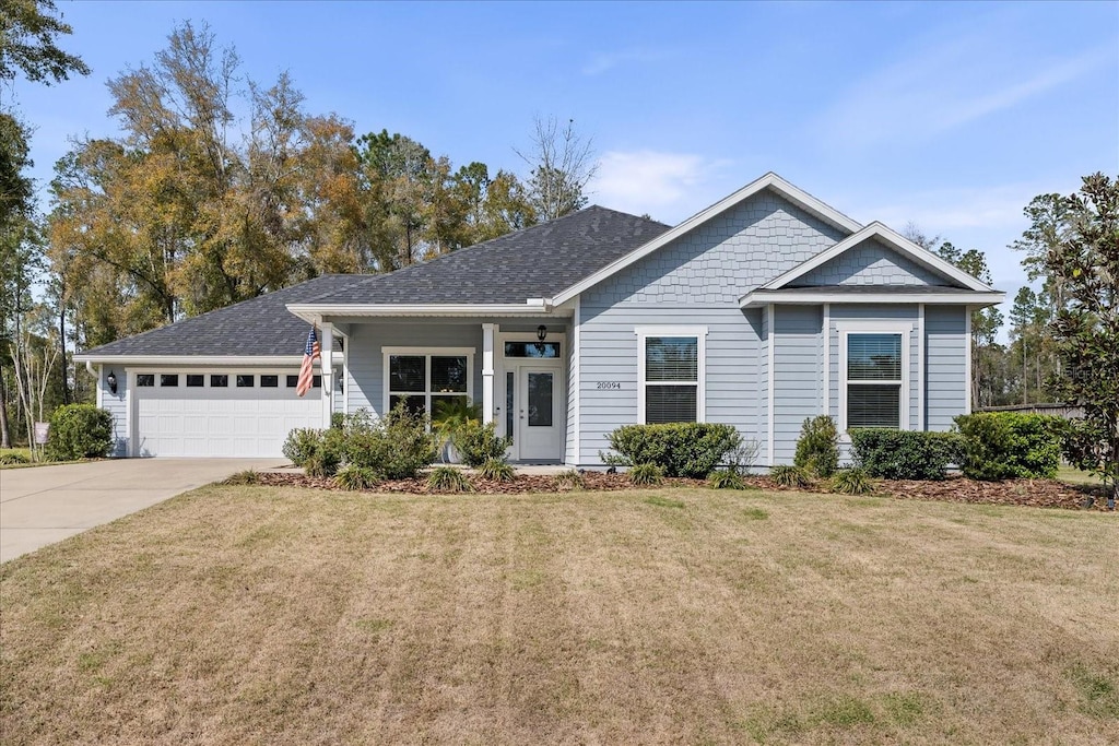 view of front facade featuring a shingled roof, an attached garage, driveway, and a front lawn