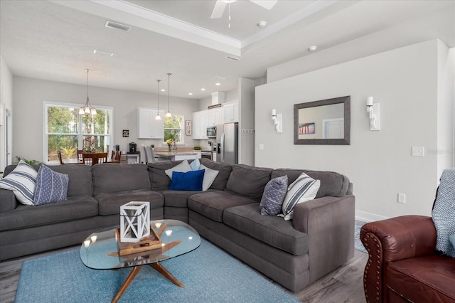 living area with ceiling fan with notable chandelier, wood finished floors, visible vents, baseboards, and a tray ceiling