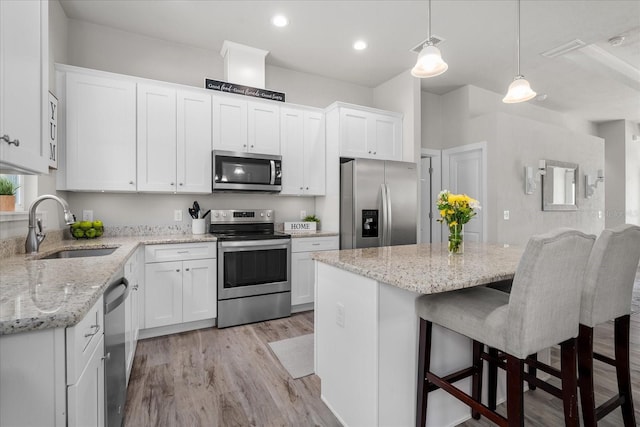 kitchen with appliances with stainless steel finishes, hanging light fixtures, a sink, white cabinetry, and a kitchen bar