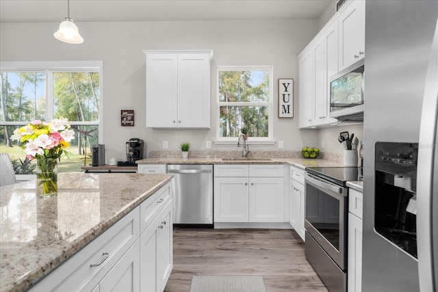 kitchen with decorative light fixtures, light wood-type flooring, a sink, stainless steel appliances, and white cabinetry