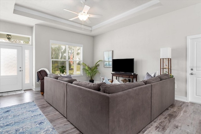 living room with baseboards, a ceiling fan, light wood-style flooring, and a tray ceiling