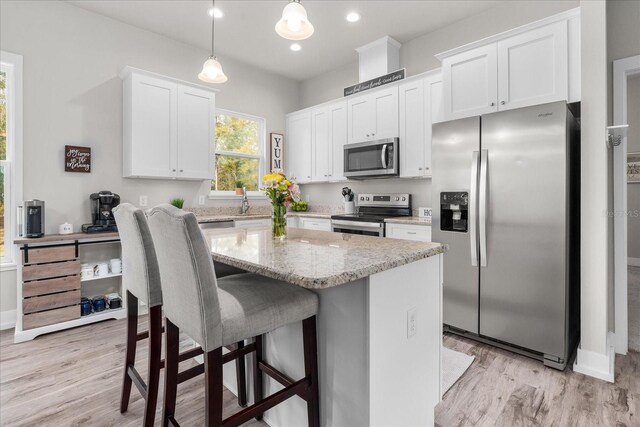 kitchen featuring a kitchen island, white cabinetry, light stone counters, light wood finished floors, and appliances with stainless steel finishes