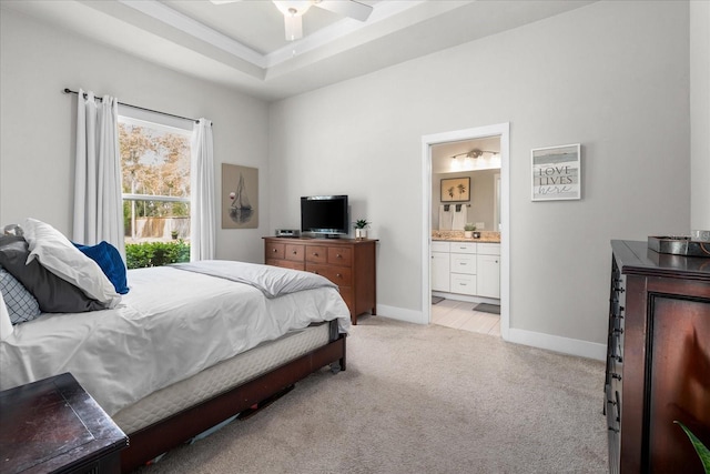 bedroom featuring baseboards, light colored carpet, a tray ceiling, and ensuite bath