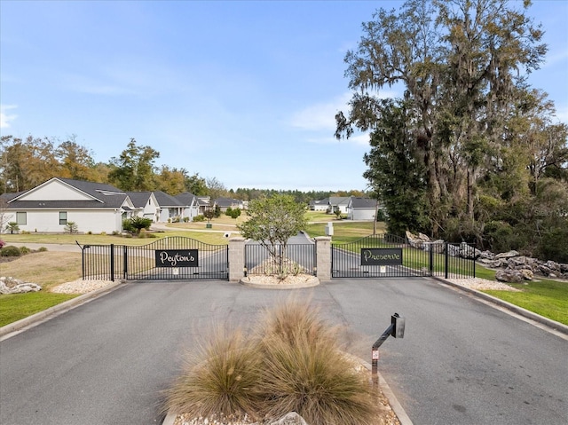 view of road with a gated entry, a residential view, a gate, and curbs