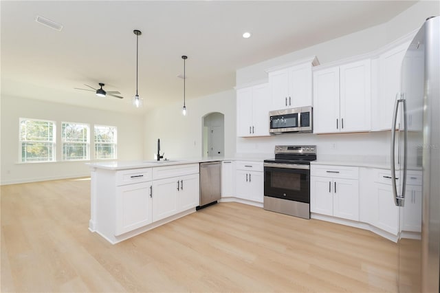 kitchen featuring stainless steel appliances, open floor plan, a sink, light wood-type flooring, and a peninsula