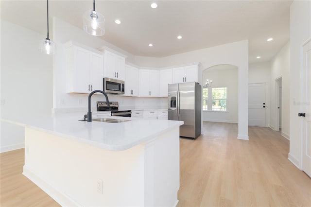 kitchen with white cabinets, appliances with stainless steel finishes, a peninsula, light countertops, and a sink