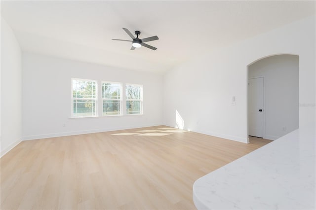 spare room with arched walkways, baseboards, a ceiling fan, and light wood-style floors