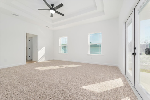 unfurnished room with a tray ceiling, light carpet, visible vents, and baseboards