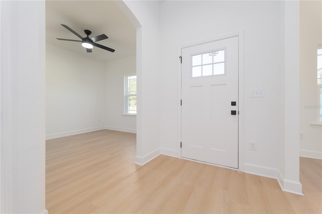 entrance foyer with light wood-style floors, baseboards, arched walkways, and a ceiling fan