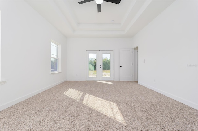 unfurnished room with light colored carpet, a raised ceiling, a healthy amount of sunlight, and french doors