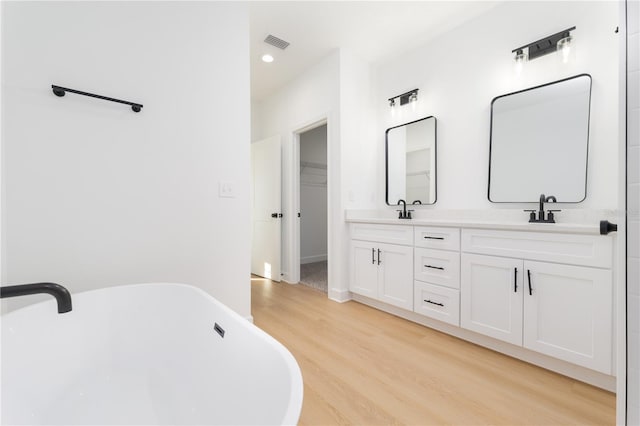 full bath featuring double vanity, visible vents, wood finished floors, a freestanding tub, and a sink