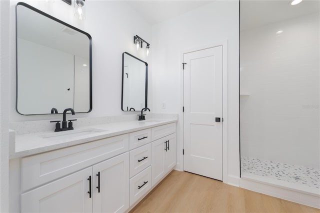 full bath featuring double vanity, wood finished floors, tiled shower, and a sink