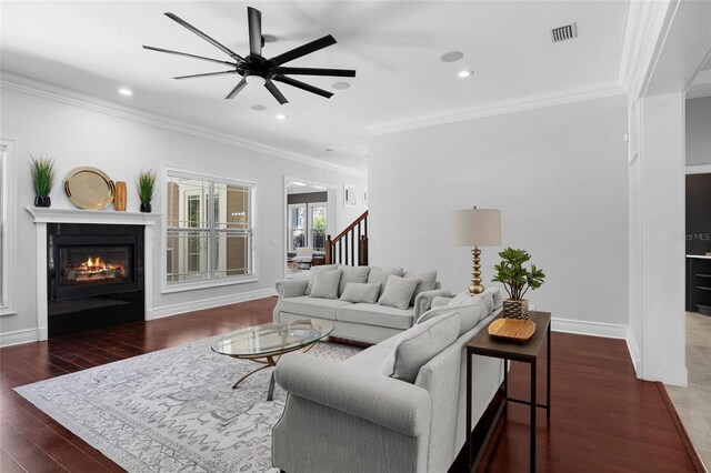 living room featuring wood finished floors, visible vents, baseboards, ornamental molding, and a glass covered fireplace