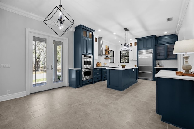 kitchen with visible vents, blue cabinets, stainless steel appliances, french doors, and wall chimney range hood