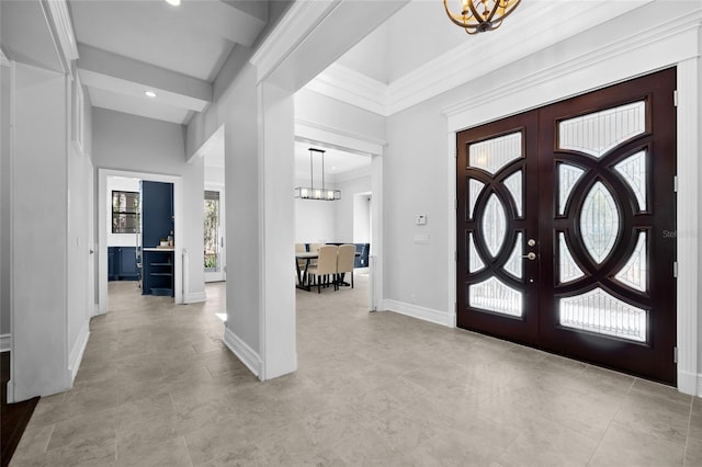 foyer with a chandelier, french doors, baseboards, and crown molding