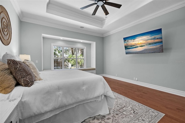 bedroom with ornamental molding, a tray ceiling, wood finished floors, and baseboards