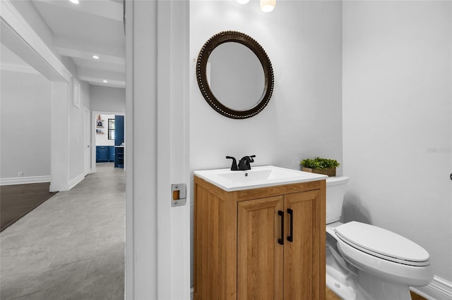 half bathroom with baseboards, vanity, and toilet