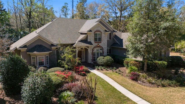 view of front of property featuring a front lawn, stone siding, and a shingled roof