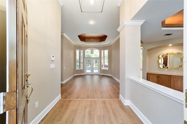 foyer entrance featuring light wood finished floors, visible vents, crown molding, decorative columns, and a raised ceiling