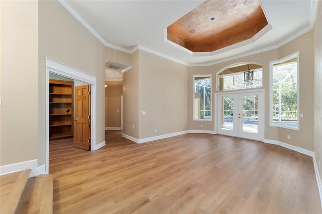 spare room featuring baseboards, light wood finished floors, a tray ceiling, french doors, and crown molding