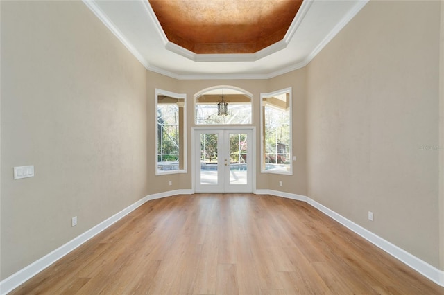 interior space featuring light wood finished floors, baseboards, a tray ceiling, ornamental molding, and french doors