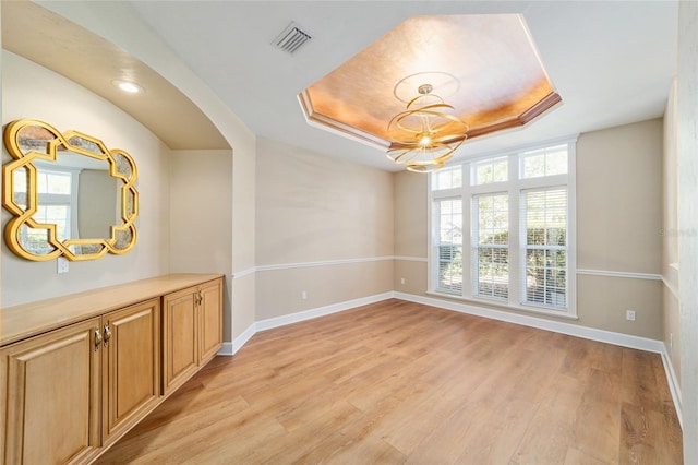 unfurnished room featuring light wood-type flooring, a raised ceiling, baseboards, and visible vents