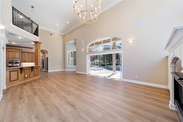 unfurnished living room featuring baseboards, a fireplace, ornamental molding, light wood-style floors, and a notable chandelier