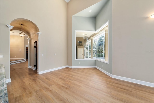 unfurnished room with an inviting chandelier, light wood-style flooring, and arched walkways