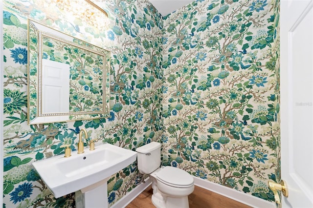 bathroom featuring toilet, wallpapered walls, baseboards, and a sink