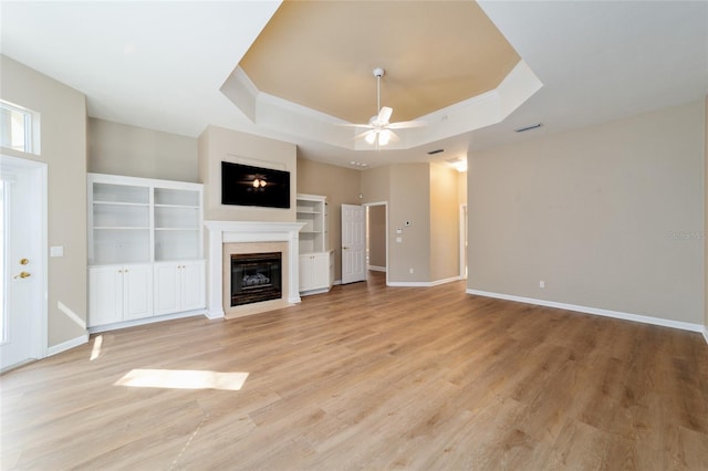 unfurnished living room featuring a tray ceiling, a fireplace with flush hearth, a ceiling fan, and light wood finished floors