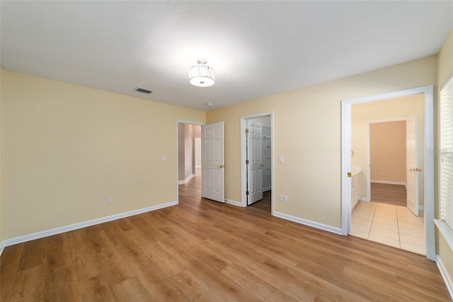 unfurnished bedroom with a spacious closet, visible vents, baseboards, and light wood-style floors