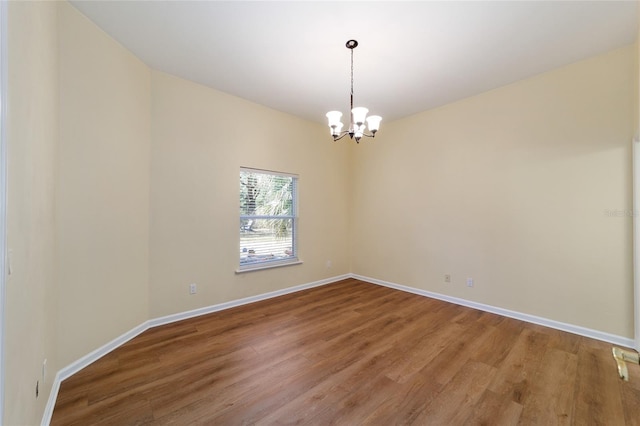 empty room featuring light wood-style flooring, a notable chandelier, and baseboards