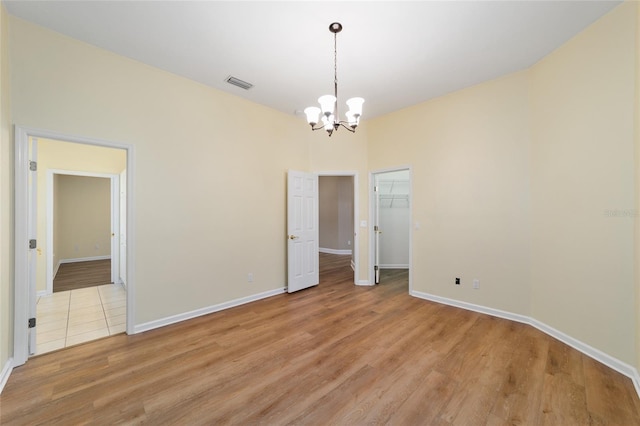 spare room featuring visible vents, baseboards, light wood-style floors, and an inviting chandelier